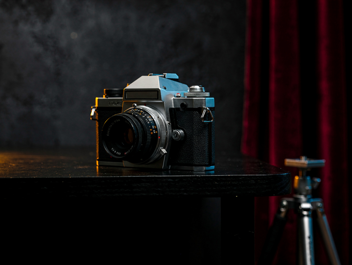 Vintage mechanical camera resting on a dark walnut table with subtle reflections